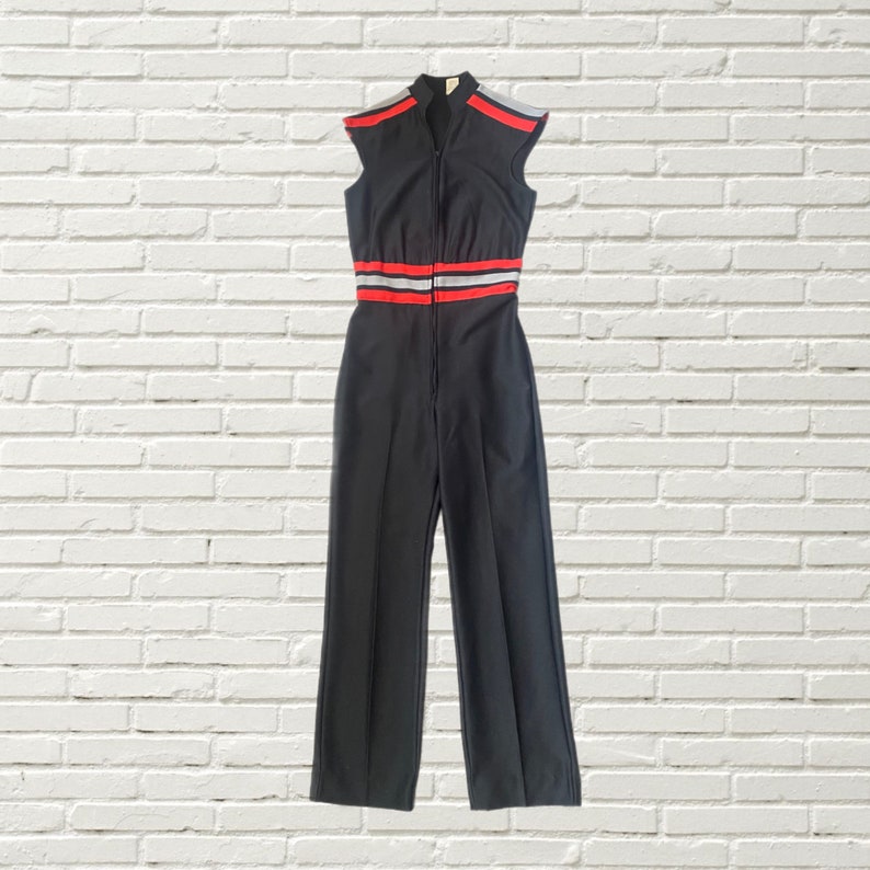 K&ouml;nnte beinhalten: Schwarzer &auml;rmelloser Jumpsuit mit einem roten und wei&szlig;en Streifen-Detail um die Taille.