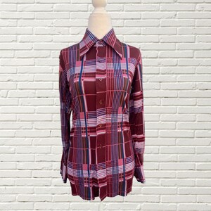 May include: A long-sleeved button-up shirt with a large plaid pattern in shades of burgundy, pink, blue, and brown. The shirt has a wide collar and a button-up front.