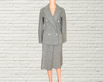 May include: A grey double-breasted blazer and skirt suit. The suit is made of a textured fabric and has a classic style.