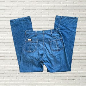 May include: A pair of blue denim jeans with a wide leg and a high waist. The jeans have a patch on the back pocket with the word "Wrangler" on it.