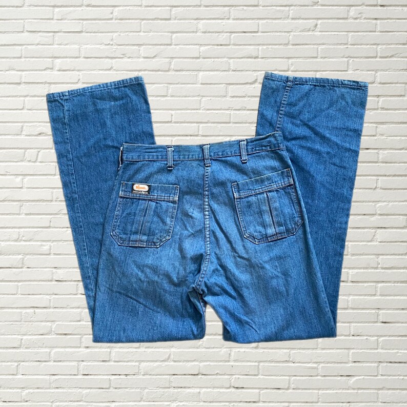 May include: A pair of blue denim jeans with a wide leg and a high waist. The jeans have a patch on the back pocket with the word "Wrangler" on it.
