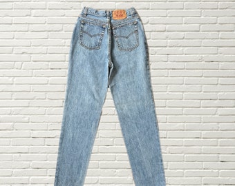 May include: Light blue denim jeans with a high waist and a straight leg. The jeans have a classic five-pocket design and a leather patch on the back with the Levi's logo.