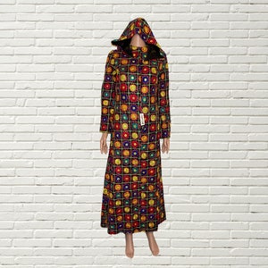 Könnte beinhalten: Ein langes schwarzes Kapuzenkleid mit einem bunten geometrischen Muster aus Kreisen und Quadraten. Das Kleid hat einen hohen Kragen und lange Ärmel.