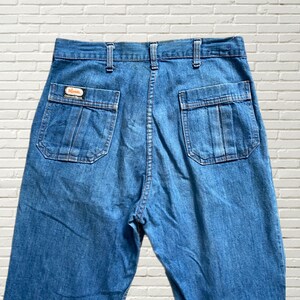 May include: A pair of blue denim jeans with a back pocket detail and a small orange label that reads "Rivet" and "Original Design".