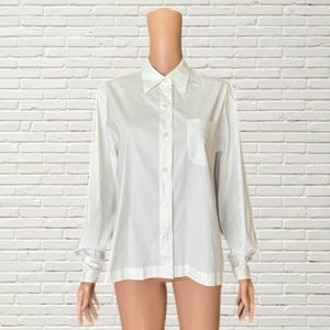 Pode incluir: Uma camisa branca de manga comprida com botões e um bolso no peito esquerdo.