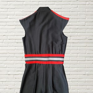 K&ouml;nnte beinhalten: Schwarzer &auml;rmelloser Jumpsuit mit einem roten und silbernen Streifen um die Taille.
