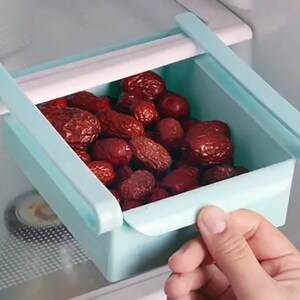 May include: A light blue plastic pull-out drawer for a refrigerator, filled with dried red fruit.