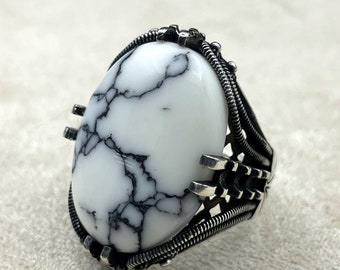 May include: A silver ring with a white oval stone featuring black veins. The ring has a detailed, intricate design.