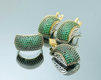May include: A set of gold-tone jewelry with green cubic zirconia stones. The set includes a ring, a pair of earrings, and a pendant.