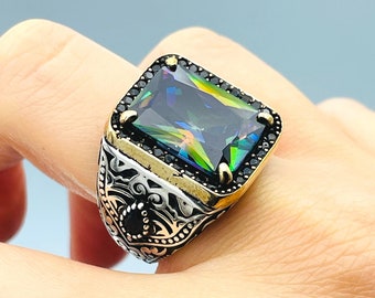 May include: A silver ring with a large, faceted, iridescent green gemstone set in a black bezel. The ring has a detailed, ornate design around the band.