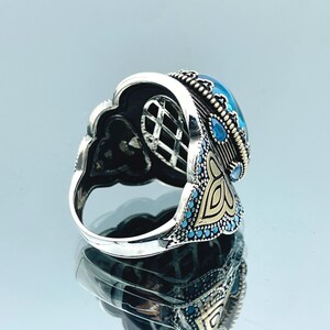 May include: A silver ring with a large blue gemstone surrounded by smaller blue gemstones. The ring has intricate gold detailing and a filigree design.