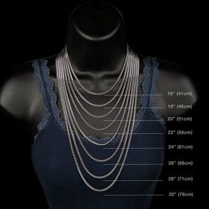 May include: A black mannequin displays a collection of silver chain necklaces of varying lengths. The necklaces range from 16 inches (41cm) to 30 inches (76cm) in length, showcasing different styles and layering options. The mannequin is wearing a navy blue tank top.