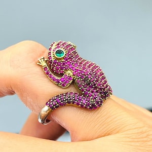 May include: A gold ring with a pink and green jeweled frog design.