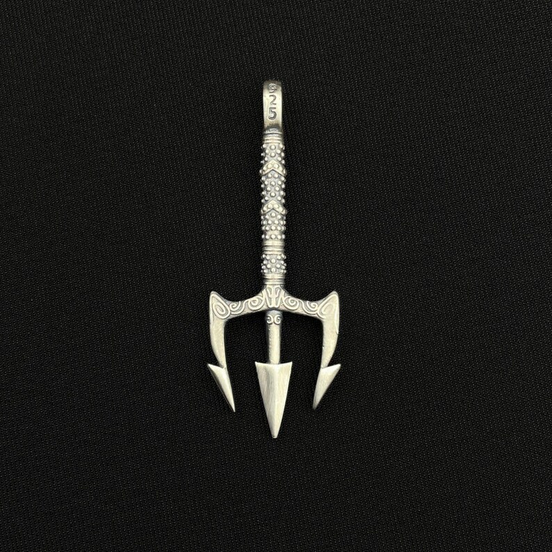 May include: A silver trident pendant with a detailed handle and three-pronged head. The pendant has a textured design and the number "925" is visible on the top. The pendant is displayed against a black background.