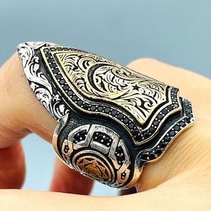 Puede incluir: Un anillo de plata y oro con un diseño de piedras negras. El anillo presenta intrincados patrones florales y una luna creciente con una estrella.