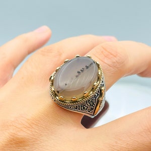 Pode incluir: Um anel de prata com uma pedra de &aacute;gata cinza engastada em uma moldura dourada. O anel &eacute; decorado com pedras de marcasita pretas ao redor da moldura e na banda.