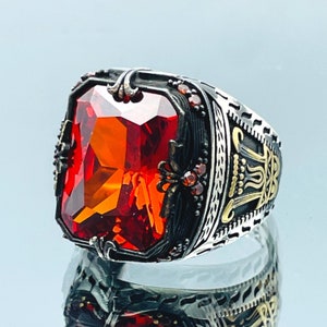 Puede incluir: Un anillo de plata con una piedra preciosa naranja engastada en un engaste detallado de plata y oro. El anillo tiene un diseño decorativo en la banda.