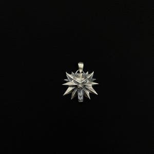 May include: A silver pendant featuring a stylized wolf's head with sharp, angular features. The pendant has a loop at the top for a chain and is set against a black background. The wolf's head has an open mouth and pointed ears.