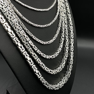 Puede incluir: Un conjunto de siete collares de cadena de plata de diferentes longitudes y anchos. Las cadenas están todas hechas en un estilo de cadena de caja, con cada eslabón encajando en el siguiente.