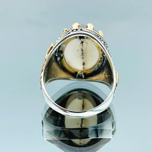 Pode incluir: Um anel de prata com uma grande pedra ovalada engastada em uma moldura de ouro. O anel &eacute; decorado com detalhes intrincados e tem uma banda de prata.