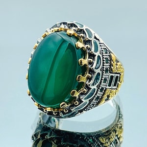 May include: A silver ring with a green gemstone set in a gold and silver crown design.
