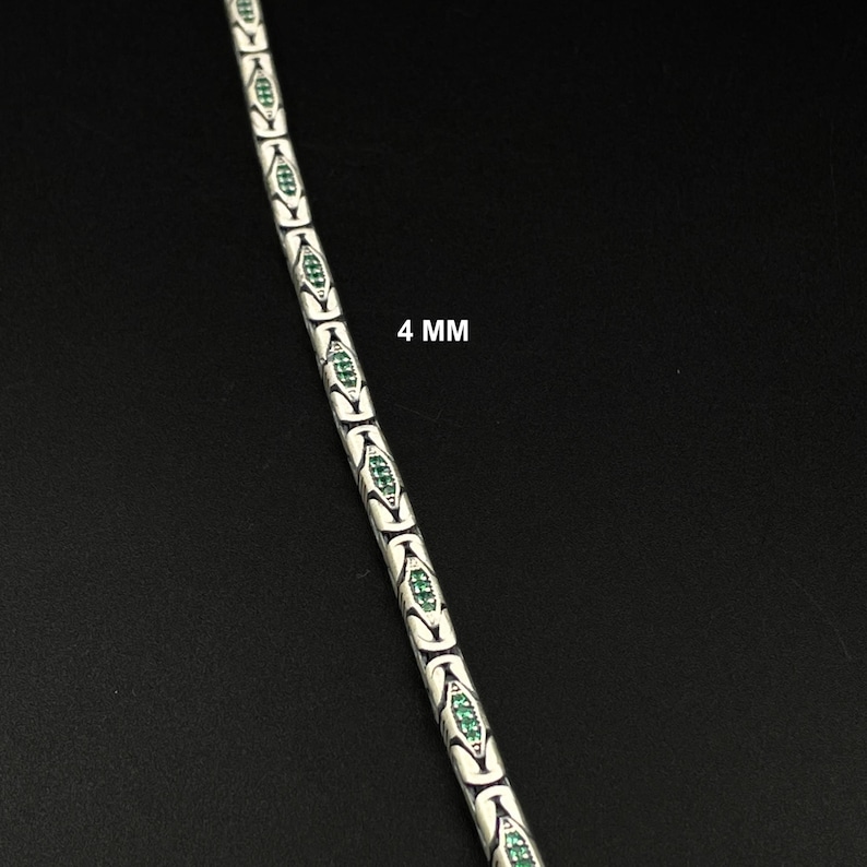 May include: A silver-colored chain bracelet with a repeating pattern of white and green oval-shaped links. The bracelet is 4 mm wide and is displayed against a black background.
