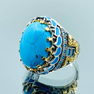 May include: A silver ring with a large turquoise stone set in a detailed design. The ring features intricate gold accents and blue enamel.