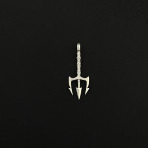 May include: A silver trident pendant with a detailed design. The pendant has a three-pronged head and a textured handle. The trident is displayed against a black background.