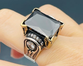 May include: A silver ring with a large black gemstone and smaller white gemstones around the setting. The ring has an ornate design with gold accents.