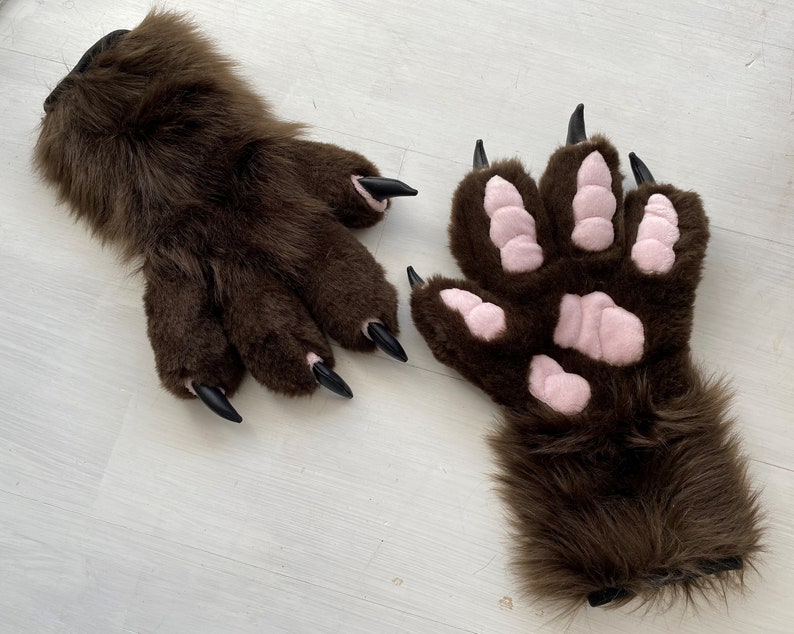 May include: A pair of brown furry paw gloves with black claws. One glove has pink paw pads.
