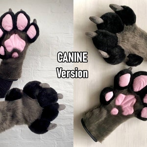 May include: A pair of gray furry paw gloves with black claws and pink paw pads. The gloves are worn by a person, and the text "CANINE Version" is visible in the background.