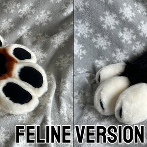 May include: A pair of brown and black furry paw hand puppets with white paw pads and pink heart-shaped details. The puppets are on a gray and white snowflake patterned fabric.