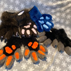 May include: Five pairs of furry paw gloves in different colors and designs. The gloves are made of soft, plush fabric and have realistic-looking claws. The colors include brown, black, gray, pink, and blue.