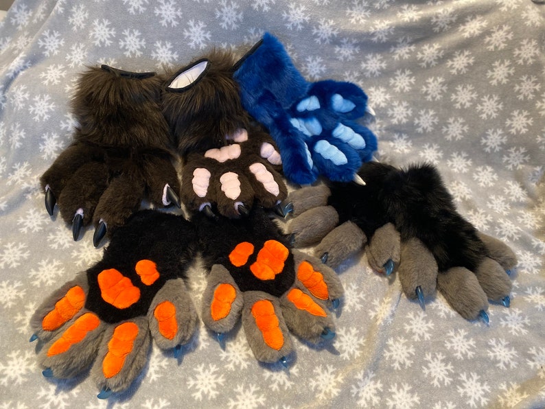 May include: Five pairs of furry paw gloves in different colors and designs. The gloves are made of soft, plush fabric and have realistic-looking claws. The colors include brown, black, gray, pink, and blue.