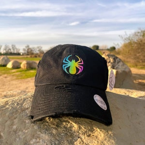 May include: Black distressed baseball cap with a rainbow spider graphic. The cap has a curved brim and an adjustable strap.