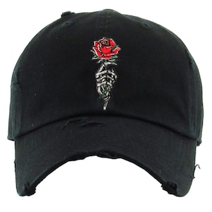 May include: Black distressed baseball cap with a red rose held by a skeleton hand graphic.
