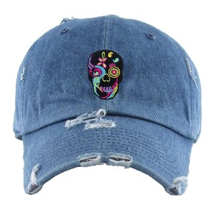 May include: A blue denim baseball cap with a distressed look and a colorful embroidered skull design on the front.