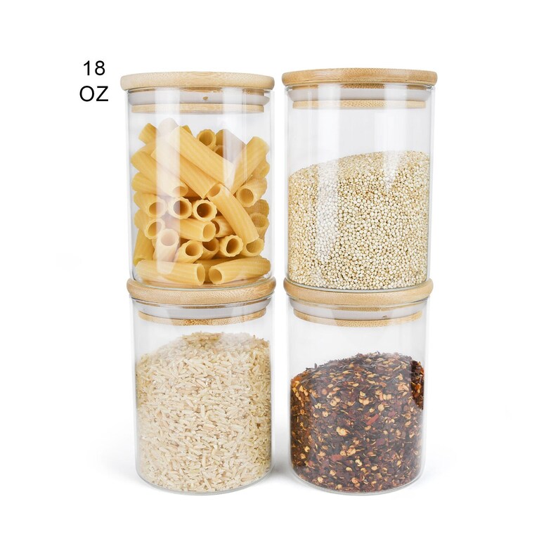May include: Four glass jars with bamboo lids, each filled with different dry goods. The jars are labeled "18 OZ". The jars contain pasta, quinoa, rice, and red pepper flakes.