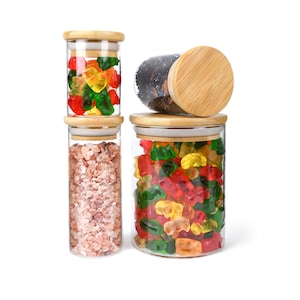 May include: Three glass jars with bamboo lids filled with various items. The top jar is filled with red, green, and yellow gummy bears. The middle jar is filled with pink Himalayan salt. The bottom jar is filled with red, green, and yellow gummy bears.