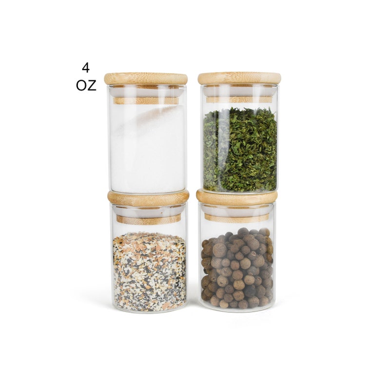 May include: Four glass jars with bamboo lids, each filled with different spices. The jars are stacked on top of each other. The jars are labeled "4 OZ".