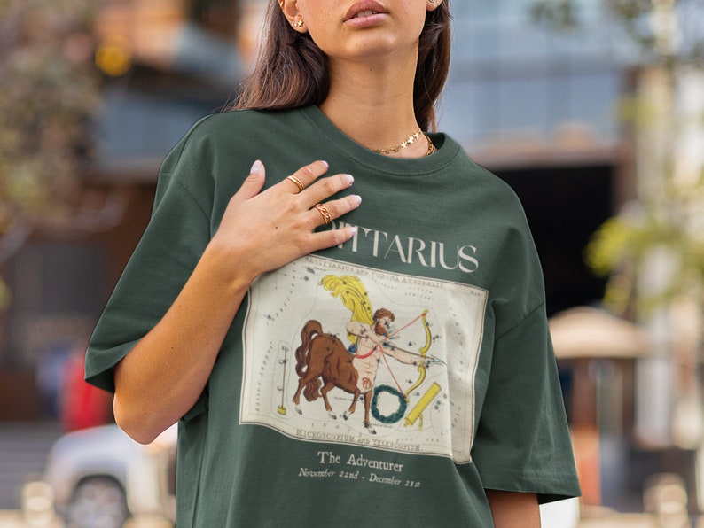 May include: A green t-shirt with a vintage illustration of the Sagittarius constellation and the text "Sagittarius, The Adventurer, November 22nd - December 21st".