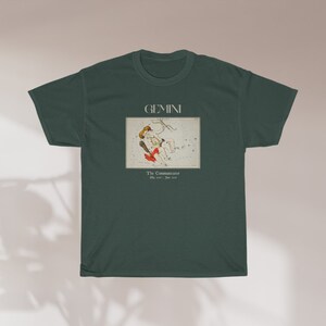 Pode incluir: Uma camiseta verde escura com um gr&aacute;fico branco da constela&ccedil;&atilde;o de G&ecirc;meos. O gr&aacute;fico inclui um desenho de duas figuras e o texto "GEMINI The Constellation May 21st - June 20th".