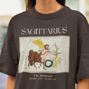 May include: A brown t-shirt with a vintage illustration of the Sagittarius constellation. The illustration is surrounded by a white border and includes the text "SAGITTARIUS", "The Adventurer", and "November 22nd - December 21st".