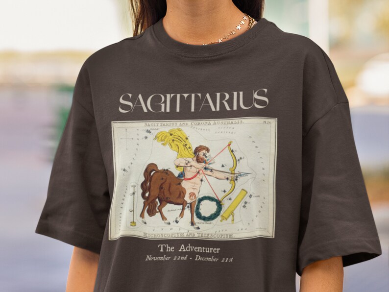May include: A brown t-shirt with a vintage illustration of the Sagittarius constellation. The illustration is surrounded by a white border and includes the text "SAGITTARIUS", "The Adventurer", and "November 22nd - December 21st".