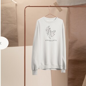 May include: White sweatshirt with a black and white line drawing of a woman dancing on a crescent moon. The text "VERIDICAL" is printed below the image.