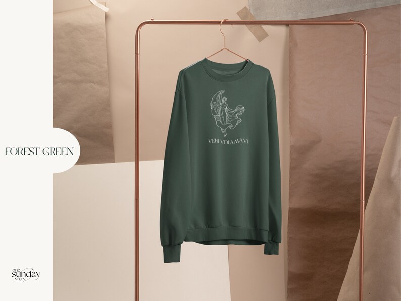 May include: Forest green sweatshirt with a white graphic of a woman dancing under a crescent moon. The text "VERIDICA AMAVI" is printed below the graphic.