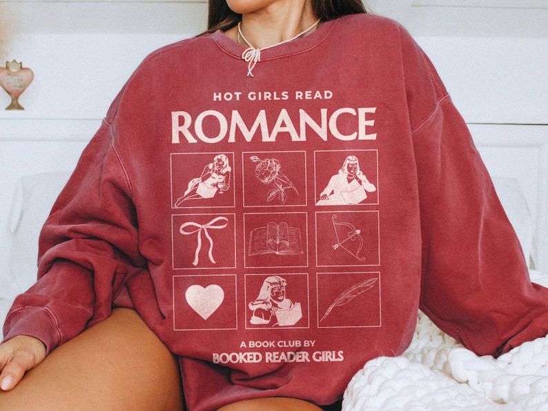 Puede incluir: Sudadera color burdeos con el texto "HOT GIRLS READ ROMANCE" y un gr&aacute;fico de nueve cuadrados con ilustraciones de una rosa, un lazo, un libro, una flecha, un coraz&oacute;n, una mujer con un libro, una pluma y dos mujeres leyendo. El texto "A BOOK CLUB BY BOOKED READER GIRLS" est&aacute; en la parte inferior.