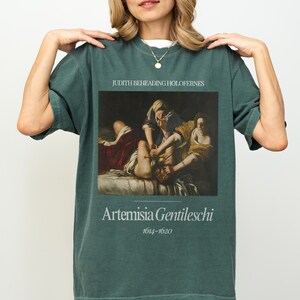 May include: A dark green t-shirt with a painting of Judith Beheading Holofernes by Artemisia Gentileschi (1614-1620).