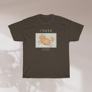 May include: A dark brown t-shirt with a graphic of the Cancer zodiac sign, a crab, and the text "Cancer, The  Nurturer, June 21st - July 22nd".