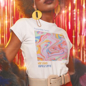 May include: A white t-shirt with a colorful abstract design and the text "Psychedelic Series" and "Retrospective" on the front. The shirt is being worn by a person with a gold belt and a fur stole.